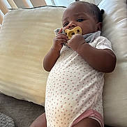 Ariana Durodola joined the competition — help win amazing prizes! baby, blanket, child, clothing, comfort, couch, cute, face, hair, hand, indoor, infant, onesie, pacifier, person, pillow, polka_dot, relaxing, skin, soft_toy