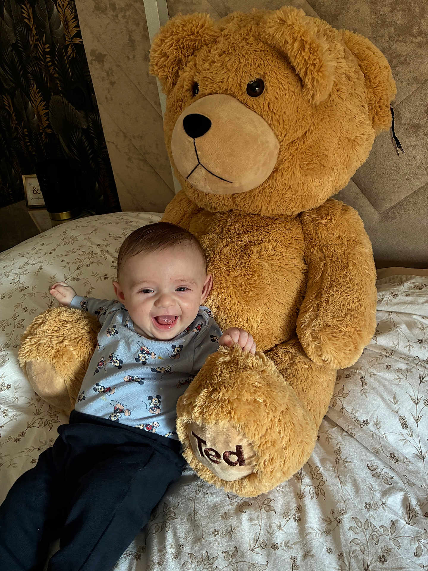 Swann participe au concours pour gagner de l'argent avec cette photo : baby, child, smiling_baby, teddy_bear, stuffed_animal, plush_toy, bed, bedding, blanket, pajamas, mickey_mouse_pattern, portrait, face, happy, cute, indoor, home_interior, clothing, sitting, toy