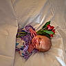 newborn, baby, infant, child, portrait, lying_down, blanket, white_bedding, purple_clothing, floral_outfit, flowers, red_flowers, green_leaves, face, hands, eyes_open, indoor, soft_lighting, close_up, photography