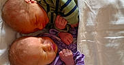 Catalina is registered to the contest to win money with this photo: newborn, twins, babies, sleeping, infants, faces, blanket, bed, portrait, indoors, cozy, peaceful, siblings, green_clothing, purple_clothing, curled_hands, closed_eyes, soft_lighting, nursery, nap