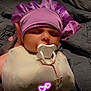 baby, bed, bodypart, bonnet, cap, clothing, costume, couch, dress, face, finger, furniture, glove, hand, hat, head, hood, newborn, person, purple