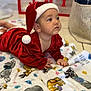 baby, basket, blanket, cat_pattern, christmas, cute, decorative_boxes, earring, face, festive, gaze, holiday, indoor, infant, joy_blocks, lying_on_stomach, portrait, red_outfit, santa_hat, soft_focus