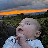 Trenton joined the competition — help win amazing prizes! baby, infant, outdoor, sunset, sky, clouds, nature, landscape, grass, greenery, person, face, expression, curious, young_child, blue_eyes, white_clothing, star_pattern, hand, scenery