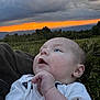 baby, infant, outdoor, sunset, sky, clouds, nature, landscape, grass, greenery, person, face, expression, curious, young_child, blue_eyes, white_clothing, star_pattern, hand, scenery