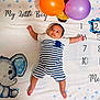 baby, infant, striped_clothing, balloons, blanket, elephant_cartoon, numbers, months, milestone, cute, child, lying_down, blue, orange, purple, portrait, celebration, young_child, indoors, soft_texture