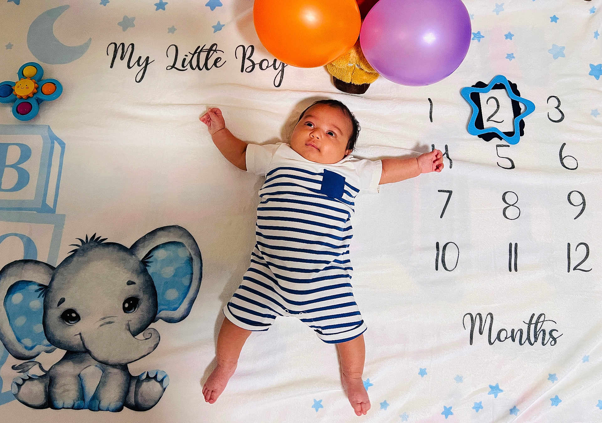 John joined the competition — help win amazing prizes! baby, infant, striped_clothing, balloons, blanket, elephant_cartoon, numbers, months, milestone, cute, child, lying_down, blue, orange, purple, portrait, celebration, young_child, indoors, soft_texture