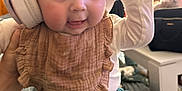 Maïley a rejoint le concours — aidez-le/la à gagner de superbes lots ! baby, headphones, bib, indoor, child, cute, clothing, person, smiling, sitting, infant, face, hand, expression, young, cozy, home, curious, apparel, candid
