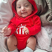 Enoch is registered to the contest to win money with this photo: baby, infant, red_hoodie, crown_graphic, smile, face, hand, sock, blanket, soft_texture, cozy, cute, child, clothing, portrait, indoors, happy, resting, comfort, person