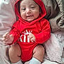baby, infant, red_hoodie, crown_graphic, smile, face, hand, sock, blanket, soft_texture, cozy, cute, child, clothing, portrait, indoors, happy, resting, comfort, person