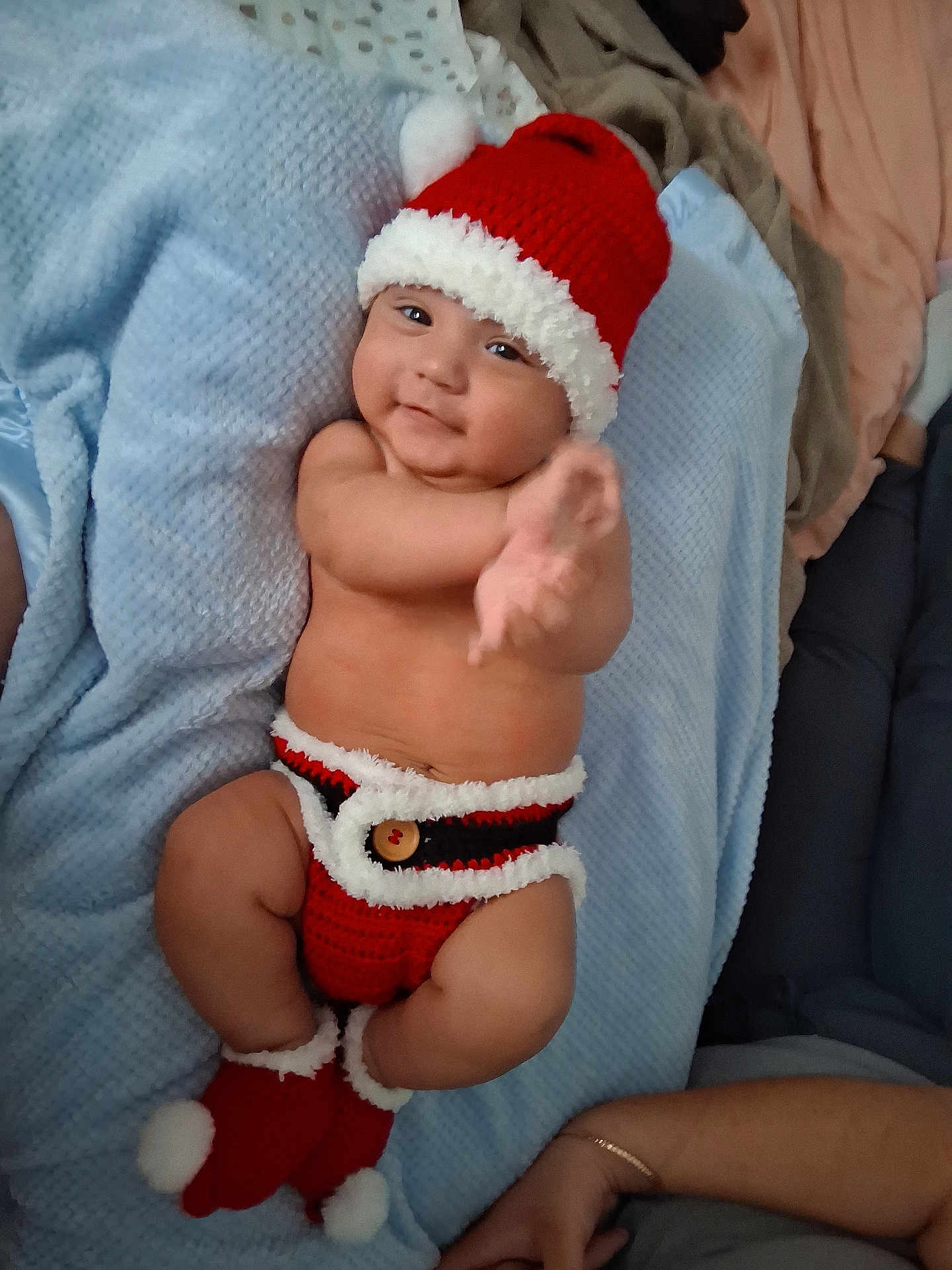 Enoch joined the competition — help win amazing prizes! baby, infant, child, knit_hat, knit_clothing, red_clothing, white_trim, blanket, soft_texture, lying_down, reaching_hand, smiling, cute, holiday_theme, santa_hat, baby_booties, person, arm, human_skin, indoors