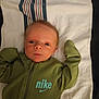 baby, infant, child, towel, green_clothing, nike_logo, face, eyes, hands, lying_down, portrait, indoor, fabric, zipper, head, skin, person, newborn, expression, cute