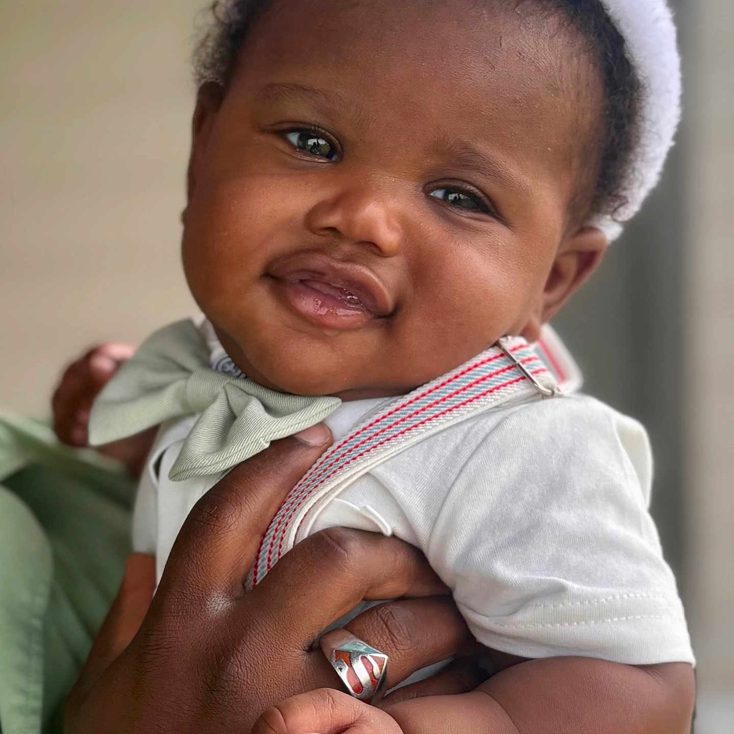 Christopher is registered to the contest to win money with this photo: baby, child, smiling, bunny_ears, bow_tie, hand, ring, portrait, cute, infant, holding, white_shirt, closeup, happy, face, person, skin, expression, indoor, adorable