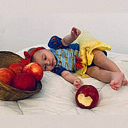Giulia participe au concours pour gagner de l'argent avec cette photo : baby, child, infant, apple, basket, bite, costume, dress, yellow_skirt, blue_top, red_bow, lying_down, white_background, soft_surface, fruit, hand, foot, cute, indoor, portrait