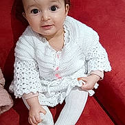 Eline a rejoint le concours — aidez-le/la à gagner de superbes lots ! baby, infant, toddler, sitting, red_couch, white_knit_sweater, white_tights, hair_accessory, star_clip, big_eyes, cute, portrait, indoor, soft_blanket, hand, sock, smile, furniture, cozy, fabric_texture