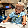 baby, bottle, cabinet, child, cute, dinosaur, expression, food_preparation, furniture, happy, high_chair, indoor, infant, kitchen, person, seat, shirt, smile, tableware, young