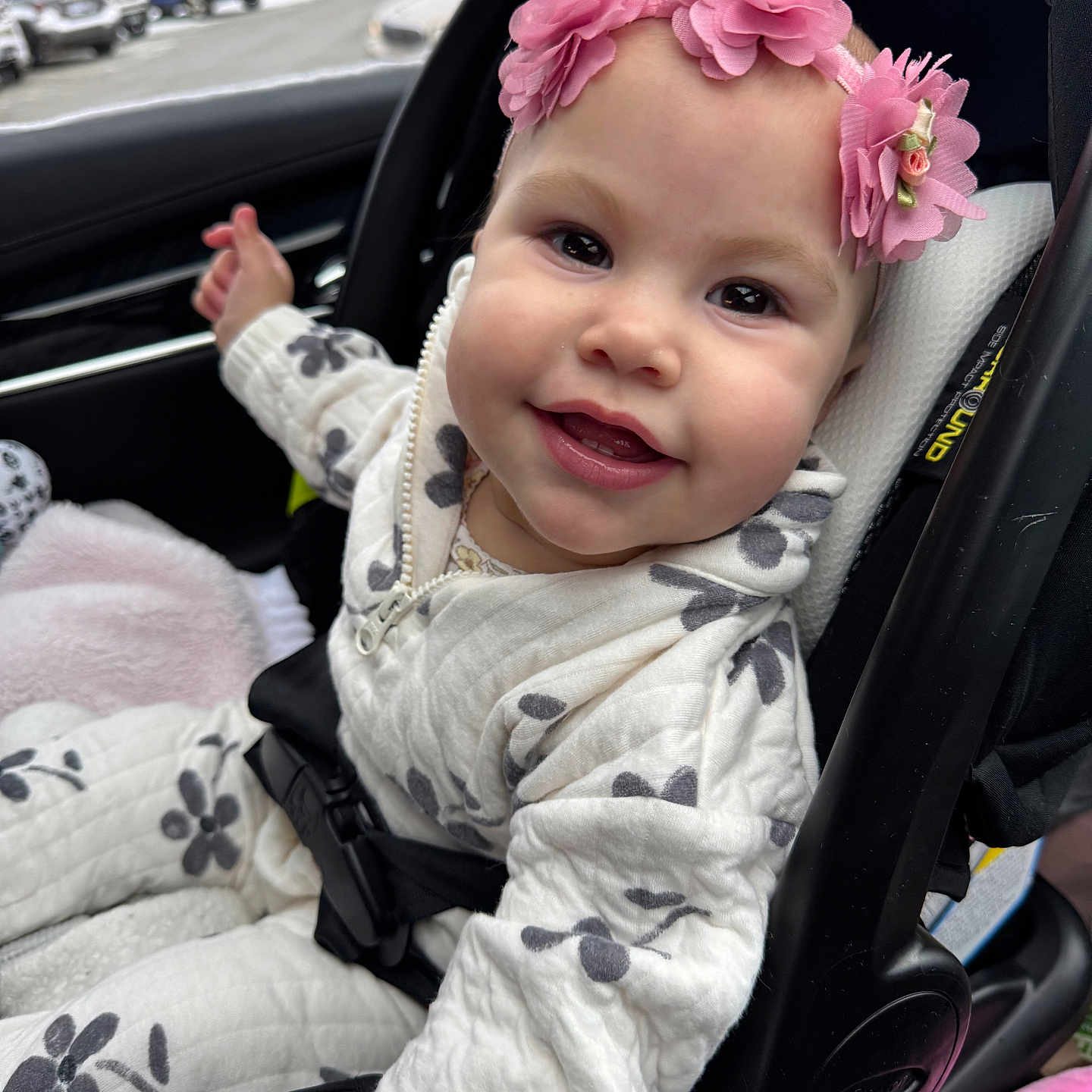 Isabella joined the competition — help win amazing prizes! baby, car_interior, car_seat, child, clothing, cute, floral_pattern, flower_headband, happy, indoors, infant, parking_lot, person, pink_flowers, portrait, seatbelt, smiling, white_outfit, window, young_child