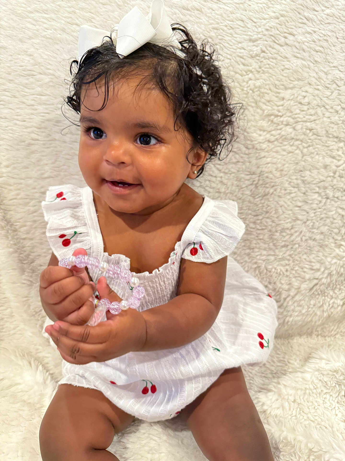 Mackenzie joined the competition — help win amazing prizes! baby, child, curly_hair, white_bow, white_dress, cherry_pattern, bracelet, beads, smiling, sitting, fluffy_blanket, cute, portrait, adorable, infant, happy, closeup, indoors, person, skin