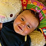 baby, smiling, infant, stuffed_animal, plush_toy, colorful_mat, child, cute, happy, face, indoor, soft_toy, black_shirt, play_mat, young_child, cuddling, portrait, lying_down, close_up, baby_boy