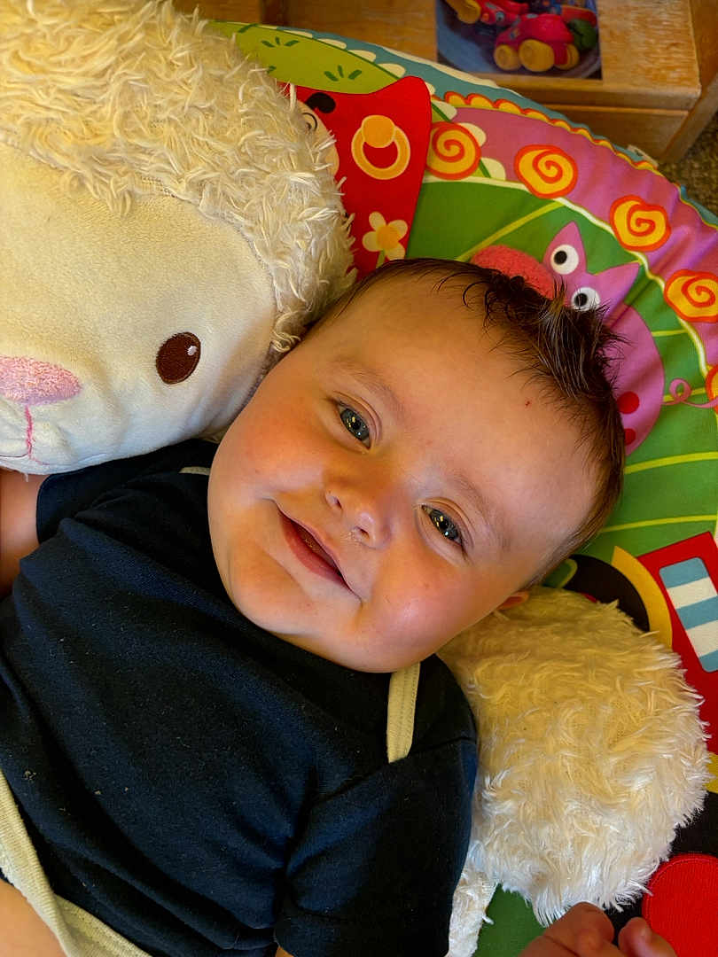 Kamryn joined the competition — help win amazing prizes! baby, smiling, infant, stuffed_animal, plush_toy, colorful_mat, child, cute, happy, face, indoor, soft_toy, black_shirt, play_mat, young_child, cuddling, portrait, lying_down, close_up, baby_boy