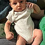 baby, infant, onesie, clothing, hand, face, skin, person, leg, foot, sitting, couch, blanket, green_shirt, indoor, soft_light, cute, newborn, expression, relaxing