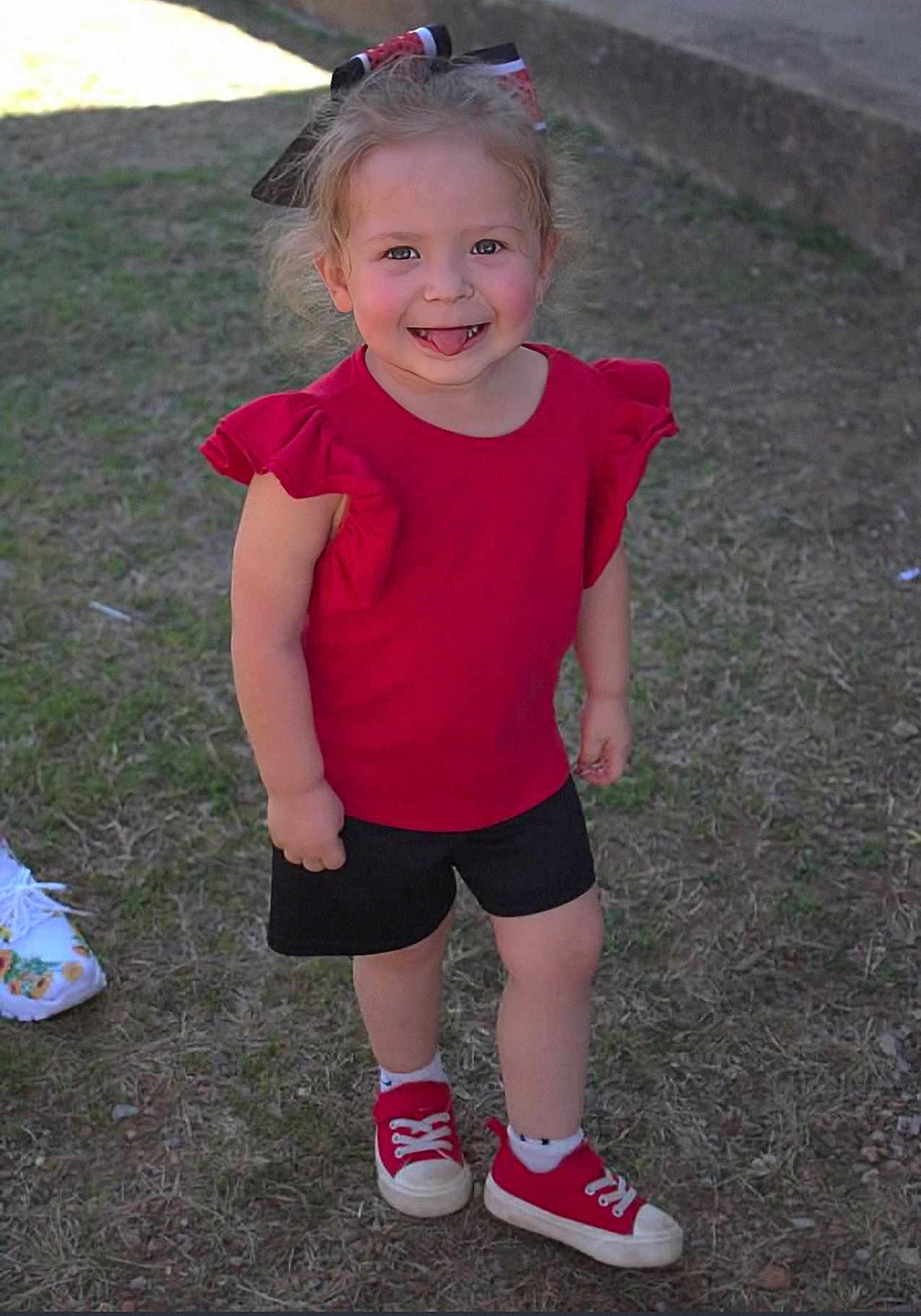 Gracee is registered to the contest to win money with this photo: toddler, child, smiling, red_shirt, black_shorts, red_sneakers, grass, outdoor, happy, bow, face, person, standing, playful, casual_clothing, young_child, cute, daylight, nature, fun