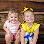 Gracee is registered to the contest to win money with this photo: casual_clothing, child, children, cute, floral_pattern, friends, girl, happy, indoor, leggings, pink_shirt, playful, portrait, sitting, smiling, two_children, wooden_background, yellow_bow, yellow_shirt, young