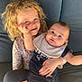 child, baby, couch, curly_hair, bib, smiling, happy, indoor, holding, clothing, person, face, sitting, window, cushion, cute, family, portrait, young_child, toddler