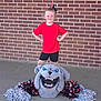 Kandie is registered to the contest to win money with this photo: child, cheerleader, red_shirt, black_shorts, pom_poms, mascot_head, bulldog, brick_wall, concrete_floor, smiling, standing, posing, outdoor, costume, team_spirit, young, happy, person, casual_clothing, sport