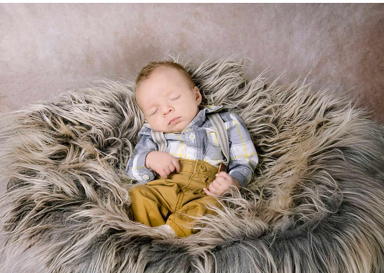 Brax is registered to the contest to win money with this photo: baby, sleeping, plaid_shirt, mustard_pants, suspenders, fur_cushion, cozy, soft_texture, indoor, portrait, peaceful, infant, child, relaxation, cute, small_hands, head, closed_eyes, rest, comfortable