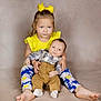 Brax is registered to the contest to win money with this photo: child, baby, toddler, sibling, portrait, yellow_bow, yellow_top, plaid_shirt, brown_pants, suspenders, barefoot, leggings, floral_pattern, studio, seated, holding, cute, family, smile, indoor