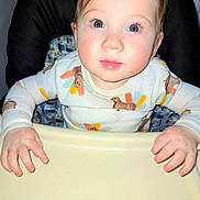 Callum is registered to the contest to win money with this photo: baby, child, high_chair, turkey_outfit, clothing, face, hands, table, curious, indoors, person, cute, skin, eyelashes, young_child, feeding_chair, expression, holiday, portrait, seated