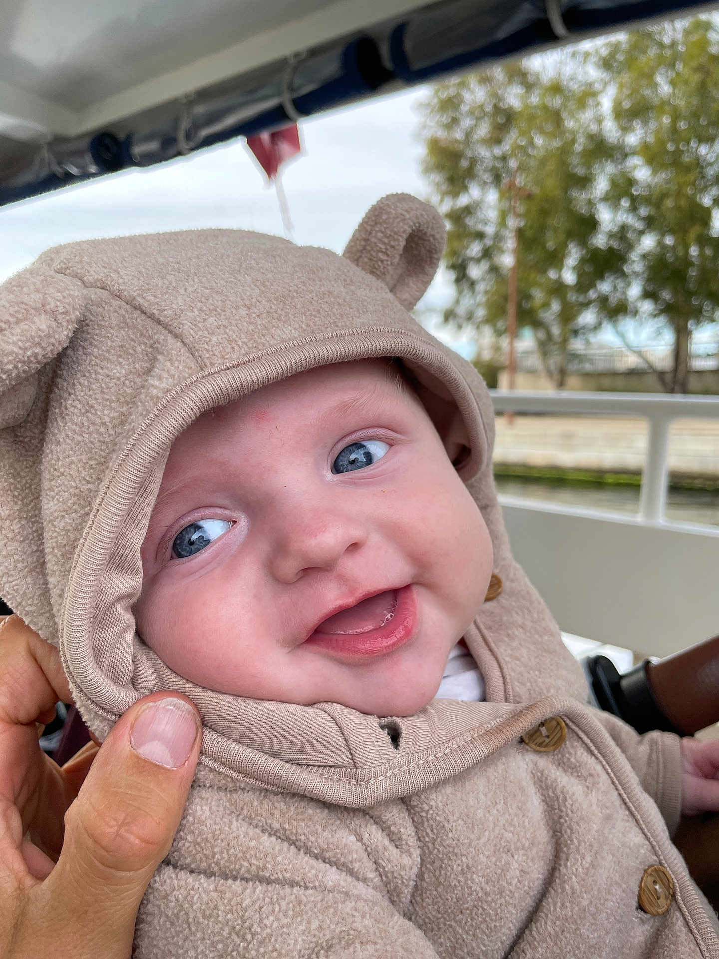 Antonin a rejoint le concours — aidez-le/la à gagner de superbes lots ! baby, child, hoodie, smile, blue_eyes, cute, outdoor, hand, person, face, clothing, button, tree, railing, happy, portrait, infant, warm_clothing, cozy, expression