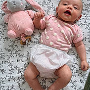 Alba a rejoint le concours — aidez-le/la à gagner de superbes lots ! arm, baby, blanket, child, cute, diaper, face, floral_pattern, hand_holding, happy, head, indoors, infant, legs, lying_down, pink_clothing, plush_toy, smiling, soft_toy, toddler