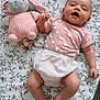 arm, baby, blanket, child, cute, diaper, face, floral_pattern, hand_holding, happy, head, indoors, infant, legs, lying_down, pink_clothing, plush_toy, smiling, soft_toy, toddler
