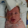 Olivia is registered to the contest to win money with this photo: newborn, baby, infant, face, portrait, hospital, swaddled, blanket, pink, bow, headband, medical_tube, bedding, lying_down, awake, winking, open_mouth, indoors, photography, cute