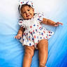 Zara Isabella joined the competition — help win amazing prizes! baby, child, infant, smiling, portrait, lying_down, blue_blanket, dress, headband, bow, red_white_blue, patriotic, fashion, cute, happy, face, hands, feet, indoor, photography