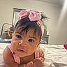 baby, infant, child, portrait, face, eyes, hair, pink_bow, headband, smiling, bed, blanket, bedroom, indoors, sitting, lying_down, bracelet, clothing, close_up, photography