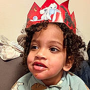 Lawson Frontin participe au concours pour gagner de l'argent avec cette photo : child, curly_hair, crown, red_crown, paper_crown, dragon, face, indoors, cozy, clothing, onesie, animal_pattern, food_on_face, couch, furniture, smiling, portrait, person, young_child, happy