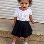 Kiara participe au concours pour gagner de l'argent avec cette photo : toddler, child, curly_hair, white_tshirt, black_skirt, white_shoes, socks, outdoor, standing, garage_door, concrete, pebbled_ground, casual_clothing, portrait, young_child, smiling, person, daylight, looking_at_camera, cute