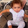 Kiara a rejoint le concours — aidez-le/la à gagner de superbes lots ! child, toddler, curly_hair, chair, outdoor, pajamas, patterned_clothing, wicker_chair, metal_chair, patio, table, plant, expression, person, sitting, young_child, daylight, casual, curly_hair_child, smiling