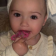 Kiara a rejoint le concours — aidez-le/la à gagner de superbes lots ! baby, child, pacifier, headband, bow, knitted_sweater, cream_color, indoor, closeup, hand, face, eyes, cute, infant, portrait, clothing, sitting, furniture, soft_lighting, young