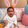 Khalaya joined the competition — help win amazing prizes! baby, child, infant, smiling, happy, sitting, portrait, easter, bunny_ears, carrot, headband, white_clothing, pajamas, colorful_eggs, easter_eggs, pillows, stuffed_decorations, indoor, playroom, celebration