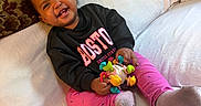 Khalaya joined the competition — help win amazing prizes! baby, child, smiling, sitting, couch, pillow, blanket, toy, rattle, sweatshirt, leggings, socks, curly_hair, portrait, indoors, home, furniture, happy, playful, colorful