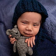 Axel joined the competition — help win amazing prizes! baby, infant, knit_hat, teddy_bear, gray_toy, blue_wrap, purple_blanket, sleepy_expression, hand, face, portrait, cozy, soft_texture, cute, child, newborn, indoor, warm_clothing, smirk, cuddle