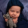baby, infant, knit_hat, teddy_bear, gray_toy, blue_wrap, purple_blanket, sleepy_expression, hand, face, portrait, cozy, soft_texture, cute, child, newborn, indoor, warm_clothing, smirk, cuddle
