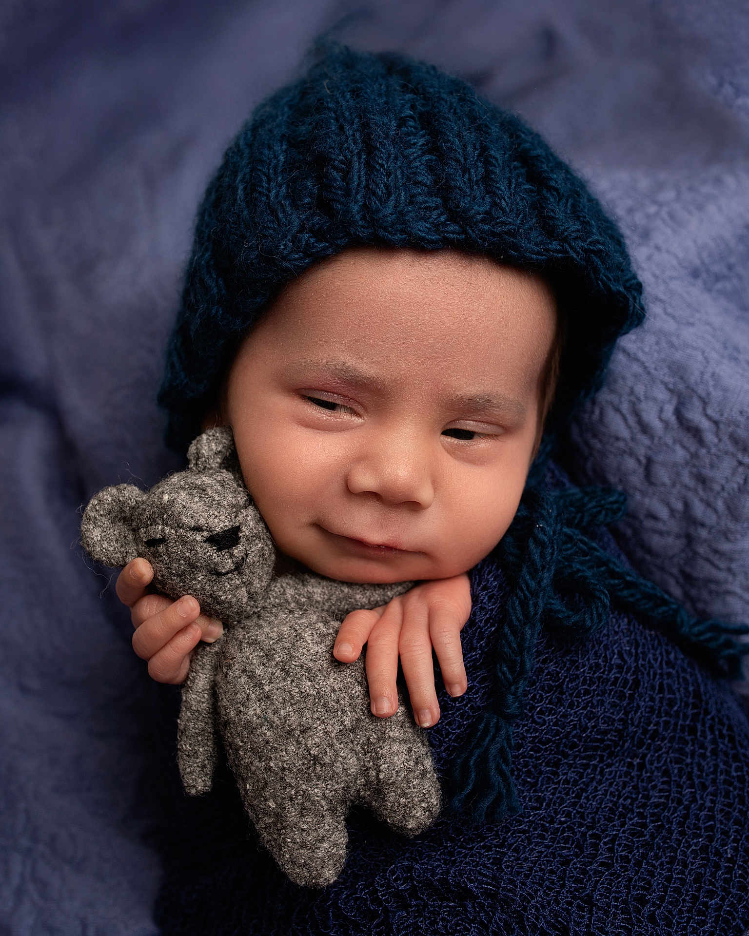Axel joined the competition — help win amazing prizes! baby, infant, knit_hat, teddy_bear, gray_toy, blue_wrap, purple_blanket, sleepy_expression, hand, face, portrait, cozy, soft_texture, cute, child, newborn, indoor, warm_clothing, smirk, cuddle