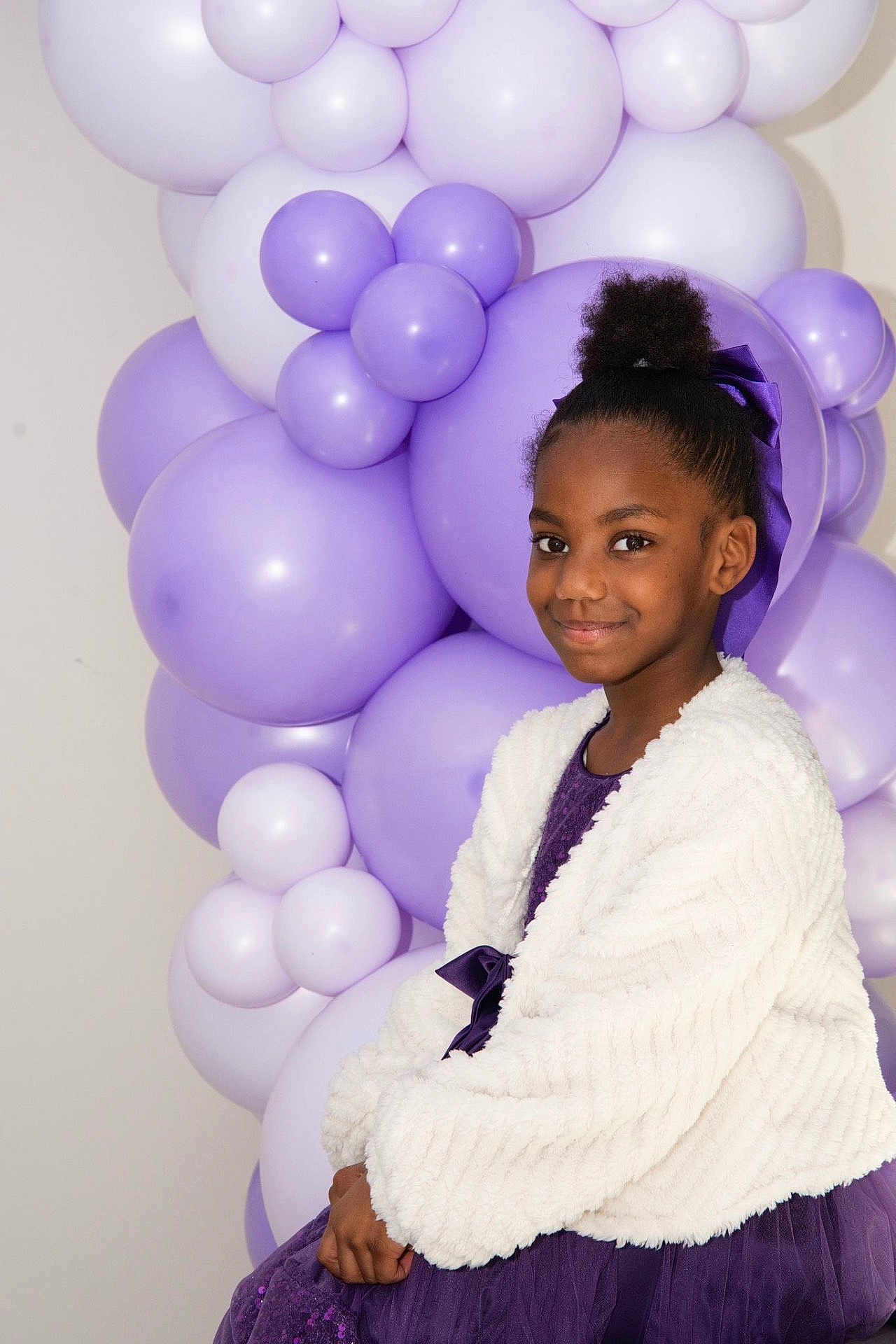 Luna Lopes a rejoint le concours — aidez-le/la à gagner de superbes lots ! child, girl, balloons, purple, dress, smile, portrait, party, celebration, bow, hair_bun, jacket, white_jacket, decor, indoor, cheerful, looking_at_camera, sitting, studio_lighting, background