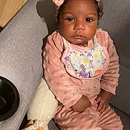 Luisa participe au concours pour gagner de l'argent avec cette photo : baby, bib, blanket, child, couch, curious_expression, dark_eyes, hand, headband, home, indoor, infant, pillow, pink_outfit, plush_toy, portrait, relaxed, sitting, textured_fabric, warm_lighting