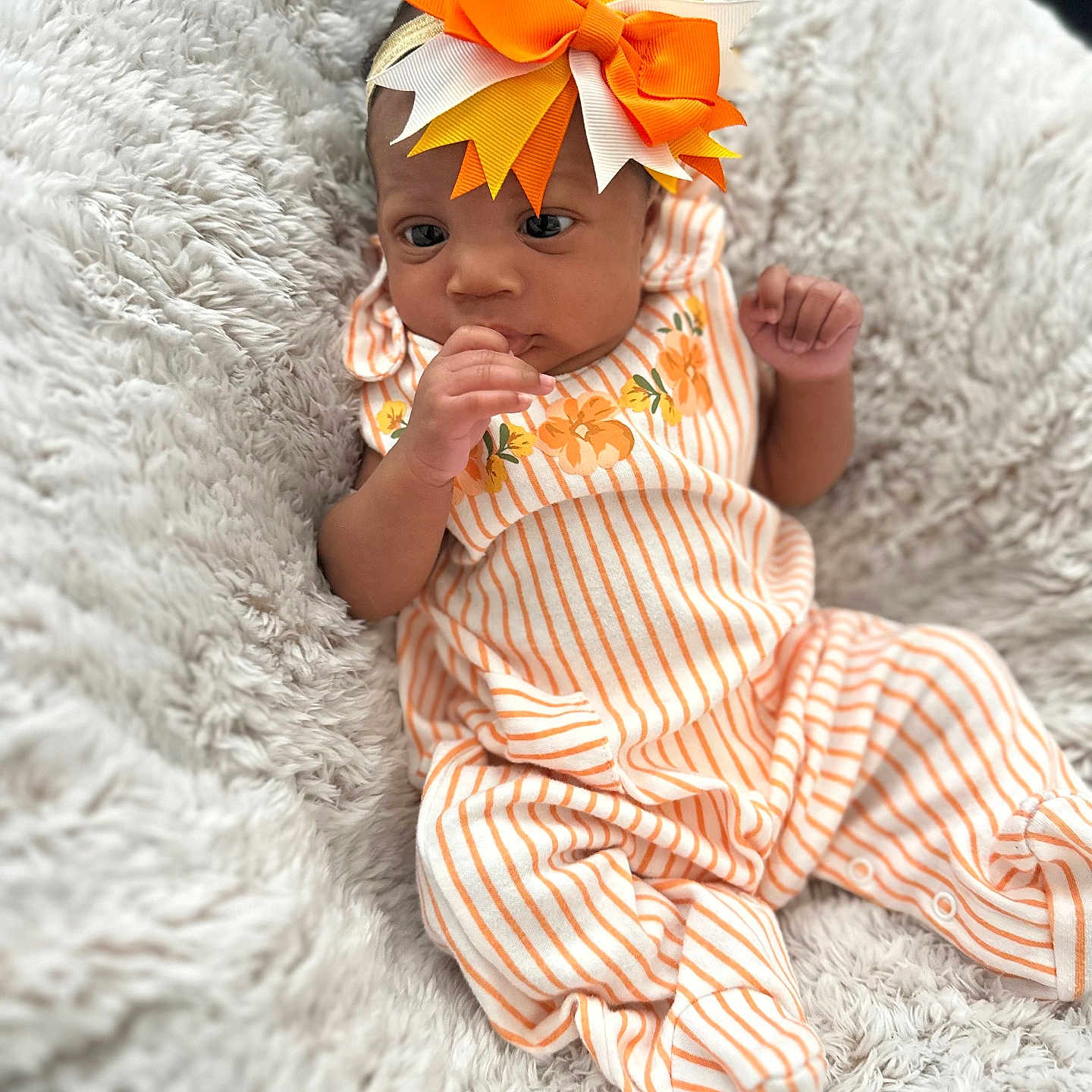 Emorie joined the competition — help win amazing prizes! baby, blanket, child, comfortable, cozy, cute, expression, floral_pattern, footed_pajamas, headband, human, indoors, infant, newborn, orange_bow, portrait, relaxed, small_hands, soft_texture, striped_clothing
