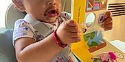 Arliss Selah is registered to the contest to win money with this photo: arm, book, bracelet, child, chocolate, clothing, curious, expression, face, hair, hand, high_chair, indoor, portrait, reading, seat, toddler, toy, wall, window